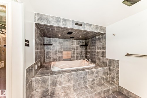Built-in soaking tub with surrounding grey square tile, recessed lighting, and wall-mounted shelves - 9845 184 Street, Edmonton, AB - Indoor Photo Showing Bathroom