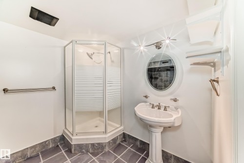 Bathroom featuring a corner shower enclosure with frosted glass, a pedestal sink, an oval mirror, and dark tile flooring - 9845 184 Street, Edmonton, AB - Indoor Photo Showing Bathroom