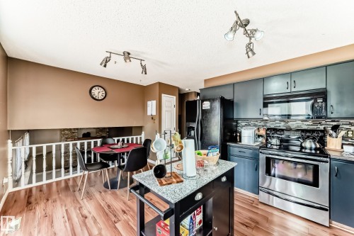 Kitchen featuring wood-finish flooring, dark cabinetry, stainless steel appliances, and a tiled backsplash - 9845 184 Street, Edmonton, AB - Indoor Photo Showing Kitchen