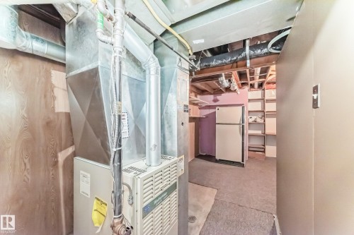 Utility area featuring a forced-air furnace, exposed ceiling joists, and a partial wall with an attached light switch - 9845 184 Street, Edmonton, AB - 
