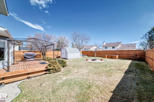 Expansive backyard featuring a wood deck, a metal gazebo frame, a gravel pathway, a storage shed, and a circular fire pit area - 9845 184 Street, Edmonton, AB - Outdoor With Deck Patio Veranda