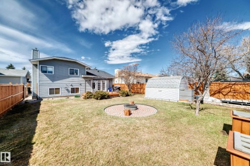 Expansive backyard featuring a brick paver fire pit area, mature trees, wood privacy fencing, and a storage shed - 9845 184 Street, Edmonton, AB - Outdoor