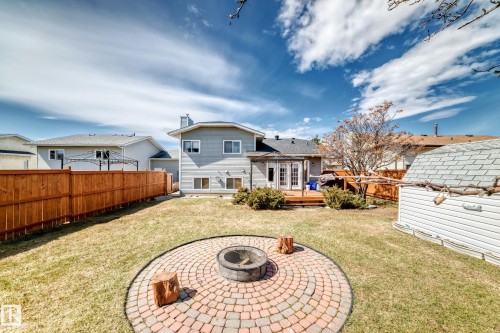 Spacious backyard featuring a circular paver patio with a built-in fire pit, a wood deck with French doors, and a durable wood fence - 9845 184 Street, Edmonton, AB - Outdoor With Deck Patio Veranda