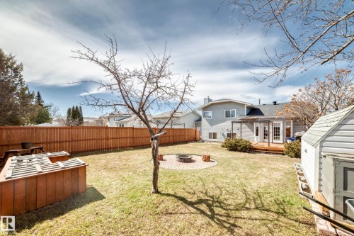 Expansive backyard featuring a manicured lawn, full privacy fencing, and a built-in fire pit with paver surround - 9845 184 Street, Edmonton, AB - Outdoor