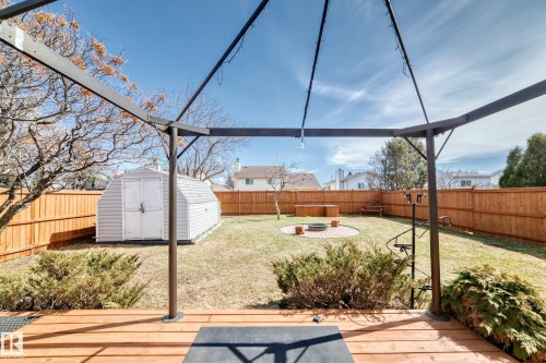 Spacious backyard featuring a wood deck, metal pergola, built-in fire pit with a paver surround, a storage shed, and a privacy fence - 9845 184 Street, Edmonton, AB - Outdoor With Deck Patio Veranda
