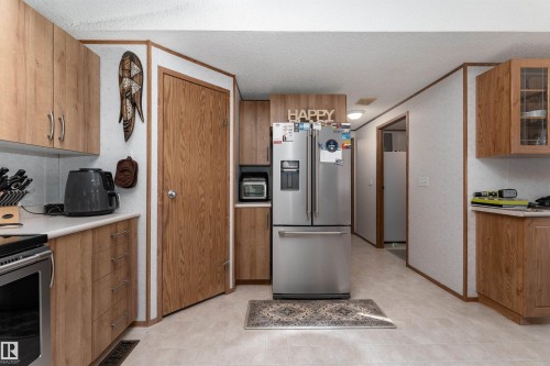 The kitchen features wood-look cabinetry, light-colored countertops, and a stainless steel refrigerator - 1663 Jubilee Crescent, Sherwood Park, AB - Indoor Photo Showing Kitchen
