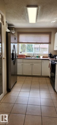Galley kitchen featuring light tile flooring, white cabinetry, a stainless steel refrigerator, and a window above the sink - 14411 31 Street, Edmonton, AB - Indoor