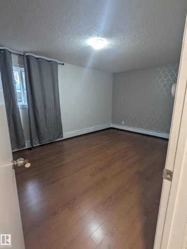 This room features hardwood flooring, a window with curtains, and a patterned accent wall - 2 9140 149 Street, Edmonton, AB - Indoor Photo Showing Other Room