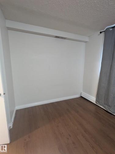 This room features dark wood-style flooring, white baseboards, and a neutral wall color - 2 9140 149 Street, Edmonton, AB - Indoor Photo Showing Other Room