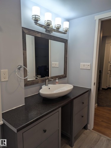 Bathroom vanity featuring a vessel sink, dark countertop, and gray cabinetry with drawers - 2 9140 149 Street, Edmonton, AB - Indoor Photo Showing Bathroom