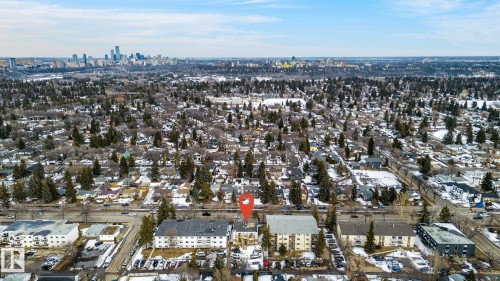 Aerial view of the property and surrounding neighborhood, featuring a cityscape in the distance, residential buildings, and numerous evergreen trees - 2 9140 149 Street, Edmonton, AB - Outdoor With View