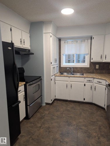 The kitchen features white cabinetry, stainless steel appliances, a double basin sink, and ample countertop space - 2 9140 149 Street, Edmonton, AB - Indoor Photo Showing Kitchen With Double Sink