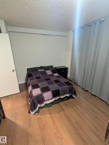 The room features light wood-style flooring, a textured ceiling, and a white door with a round handle - 2 9140 149 Street, Edmonton, AB - Indoor Photo Showing Bedroom