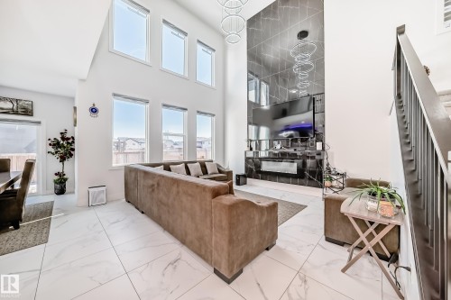 Two-story living area featuring large format white tile flooring, a dark accent wall with a built-in fireplace, and a contemporary chandelier - 17459 80 Street, Edmonton, AB - Indoor