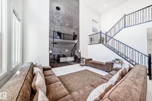Two-story living area featuring a prominent black marble-finish accent wall with integrated media console, a modern multi-ring chandelier, and large windows - 17459 80 Street, Edmonton, AB - Indoor With Fireplace