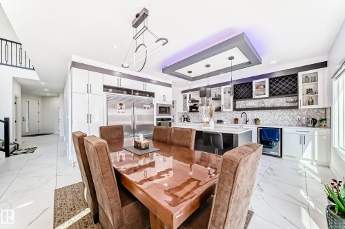 Contemporary kitchen and dining area featuring a tiered ceiling with recessed lighting, integrated stainless steel appliances, and a central island with pendant lighting - 17459 80 Street, Edmonton, AB - Indoor Photo Showing Dining Room