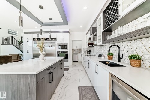 Contemporary kitchen featuring an oversized island with a white countertop, flat-panel cabinetry, a patterned tile backsplash, stainless steel appliances, and sleek pendant lighting - 17459 80 Street, Edmonton, AB - Indoor Photo Showing Kitchen With Upgraded Kitchen