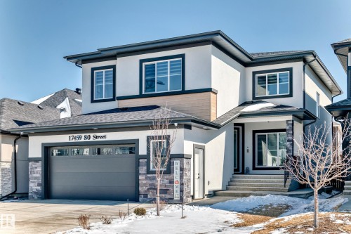 Contemporary stucco exterior featuring a covered entry, stone accents, dark trim, a two-car garage with frosted windows, and an asphalt shingle roof - 17459 80 Street, Edmonton, AB - Outdoor With Facade