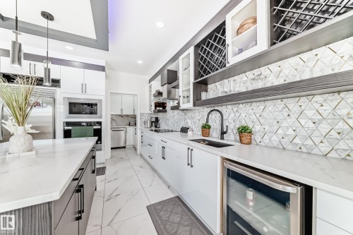 Modern kitchen featuring a large island with a waterfall countertop, integrated stainless steel appliances, a geometric tile backsplash, wine storage, and recessed lighting - 17459 80 Street, Edmonton, AB - Indoor Photo Showing Kitchen With Upgraded Kitchen
