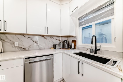 Modern kitchen featuring glossy white cabinetry with black hardware, white countertops with prominent veining, a matching veined backsplash, an undermount black sink with a gooseneck faucet, and a stainless steel dishwasher - 17459 80 Street, Edmonton, AB - Indoor Photo Showing Kitchen With Upgraded Kitchen