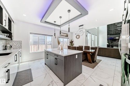 Modern kitchen and dining area featuring a central island with a quartz-style countertop, integrated cabinetry, and contemporary pendant lighting - 17459 80 Street, Edmonton, AB - Indoor Photo Showing Kitchen With Upgraded Kitchen