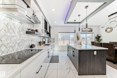Contemporary kitchen featuring a full-height triangular mosaic tile backsplash, built-in cooktop with a range hood, and white cabinetry with matte black hardware - 17459 80 Street, Edmonton, AB - Indoor Photo Showing Kitchen With Upgraded Kitchen