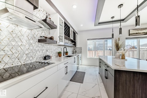 Contemporary kitchen featuring white cabinetry, a geometric tile backsplash, and a built-in cooktop with a stainless steel range hood - 17459 80 Street, Edmonton, AB - Indoor Photo Showing Kitchen With Upgraded Kitchen