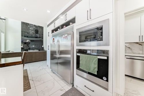 Modern kitchen featuring integrated stainless steel appliances, crisp white cabinetry with brushed nickel hardware, and large format white tile flooring - 17459 80 Street, Edmonton, AB - Indoor Photo Showing Kitchen