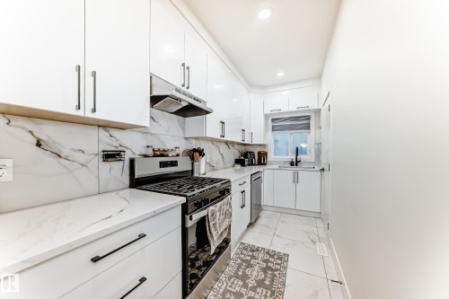 Modern kitchen featuring white cabinetry, stone-finish countertops, a gas range with a stainless steel hood, an undermount sink with a black faucet, and tiled flooring - 17459 80 Street, Edmonton, AB - Indoor Photo Showing Kitchen