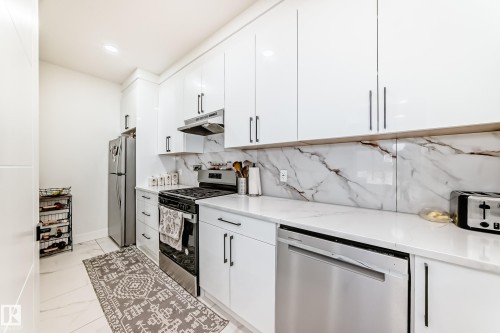 Contemporary kitchen featuring white high-gloss cabinetry with linear pulls, stainless steel appliances, and a marble-patterned backsplash - 17459 80 Street, Edmonton, AB - Indoor Photo Showing Kitchen With Upgraded Kitchen