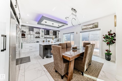 Open-concept kitchen and dining area featuring large format marble-look tile flooring, white cabinetry, a kitchen island with seating, stainless steel appliances, and sliding glass doors to the exterior - 17459 80 Street, Edmonton, AB - Indoor Photo Showing Dining Room