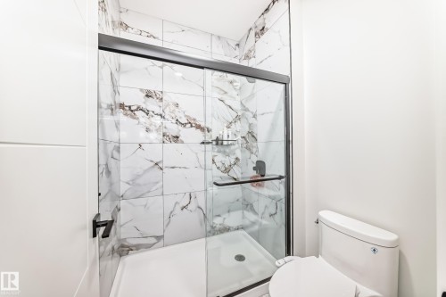 Glass-enclosed shower featuring large format tile with naturalistic veining, a matte black shower head, and a built-in corner shelf - 17459 80 Street, Edmonton, AB - Indoor Photo Showing Bathroom