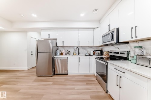 Modern kitchen featuring stainless steel appliances, white cabinetry, integrated sink with a black faucet, light wood-finish flooring, and recessed lighting - 17459 80 Street, Edmonton, AB - Indoor Photo Showing Kitchen