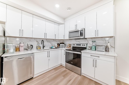 Modern kitchen featuring white cabinetry, stainless steel appliances, a black faucet, white countertops, and a white backsplash with gray veining - 17459 80 Street, Edmonton, AB - Indoor Photo Showing Kitchen