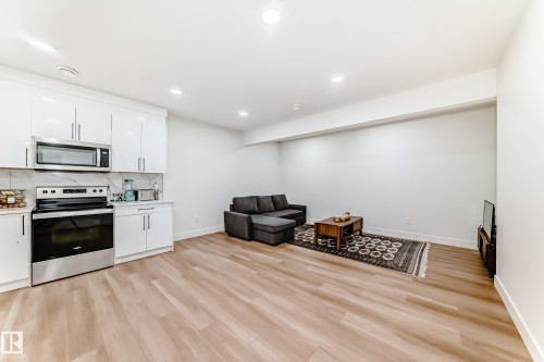 Open-concept living space featuring wood-finish flooring, recessed lighting, and a kitchen area with white cabinetry, stainless steel appliances, and a marble-finish backsplash - 17459 80 Street, Edmonton, AB - Indoor
