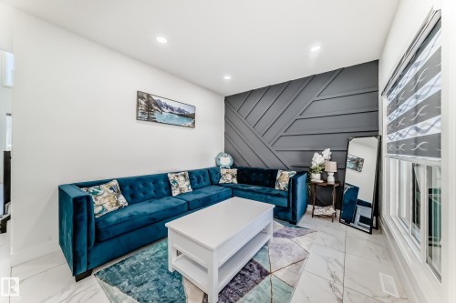 Living area featuring a textured accent wall with geometric wood paneling, white walls, recessed ceiling lighting, and large format marble-look tile flooring - 17459 80 Street, Edmonton, AB - Indoor