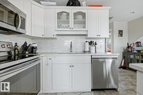 Modern kitchen featuring white cabinetry, stainless steel appliances, a white tile backsplash, a built-in microwave, and a stainless steel dishwasher - 115 10105 95 Street, Edmonton, AB - Indoor Photo Showing Kitchen With Upgraded Kitchen