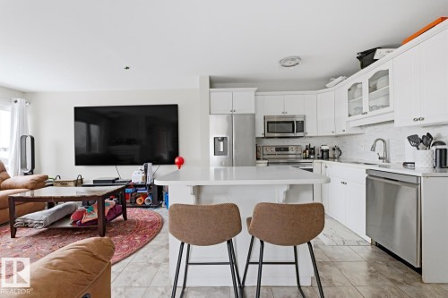Open-concept kitchen featuring white cabinetry, stainless steel appliances, a white subway tile backsplash, and a central island with a solid surface countertop - 115 10105 95 Street, Edmonton, AB - Indoor Photo Showing Kitchen