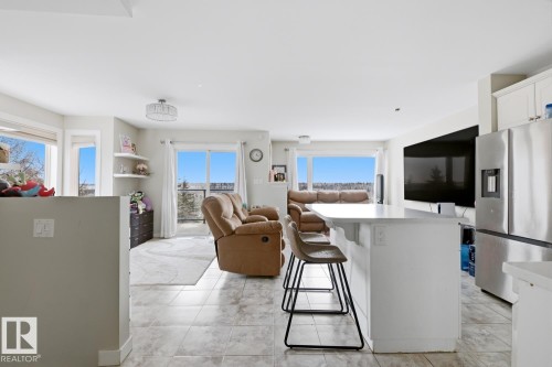 Open-concept living space featuring light tile flooring, a kitchen island with seating, stainless steel refrigerator, and dual sliding glass doors - 115 10105 95 Street, Edmonton, AB - Indoor