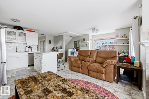 Open-concept living space with a kitchen island, white cabinetry, tile flooring, and a modern subway tile backsplash - 115 10105 95 Street, Edmonton, AB - Indoor