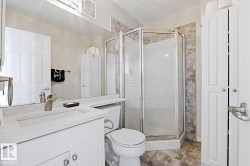 Bathroom featuring a corner shower enclosure, white vanity with integrated sink, a commode, a large wall-mounted mirror, and tile flooring - 