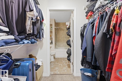 Walk-in closet with carpet flooring and direct access to a full bathroom featuring tile flooring, a built-in bathtub, and a tiled shower surround - 115 10105 95 Street, Edmonton, AB - Indoor With Storage