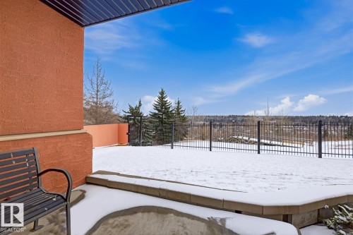 Open-air patio featuring a textured stucco exterior, a black metal fence, and a stone retaining wall - 115 10105 95 Street, Edmonton, AB - Outdoor With Exterior