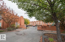 Gated residential community entrance featuring a black metal gate and a stucco-finish wall with property signage - 