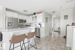 Modern kitchen featuring white cabinetry, stainless steel appliances, a white island with an integrated breakfast bar, and a patterned tile floor - 