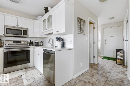 Kitchen featuring white cabinetry, stainless steel appliances, a white tile backsplash, and a corner sink - 115 10105 95 Street, Edmonton, AB - Indoor Photo Showing Kitchen