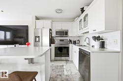 Modern kitchen featuring white cabinetry, stainless steel appliances, a white tile backsplash, and a light-toned countertop with an integrated breakfast bar - 