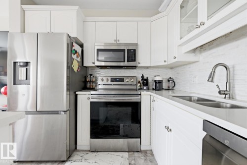 White shaker cabinetry with crown molding, stainless steel appliances, a mosaic tile backsplash, and a double basin sink with a gooseneck faucet - 115 10105 95 Street, Edmonton, AB - Indoor Photo Showing Kitchen With Double Sink