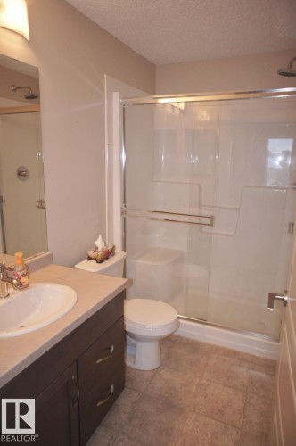 Bathroom featuring a glass-enclosed shower, a vanity with an integrated sink, a toilet, and tiled flooring - 326 6076 Schonsee Way, Edmonton, AB - Indoor Photo Showing Bathroom