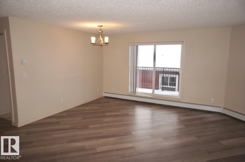 Spacious living area featuring wood-finish flooring, neutral wall tones, and a brushed nickel chandelier - 326 6076 Schonsee Way, Edmonton, AB - Indoor Photo Showing Other Room